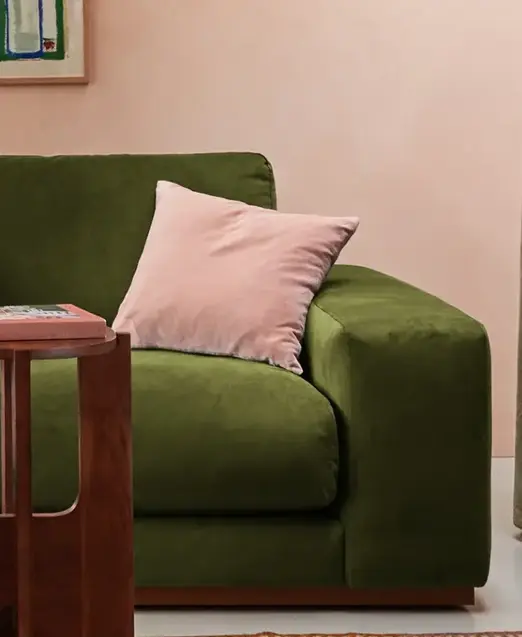 a green couch with pink pillows and a red stool