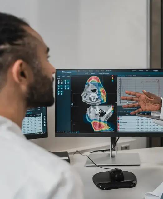 a woman in a white coat talking to a man in front of computer screens